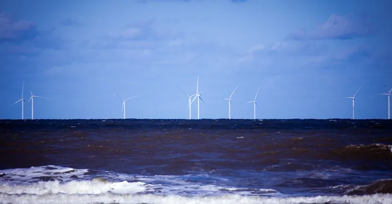 Offshore wind turbines generating sustainable energy over a calm ocean under a clear blue sky.