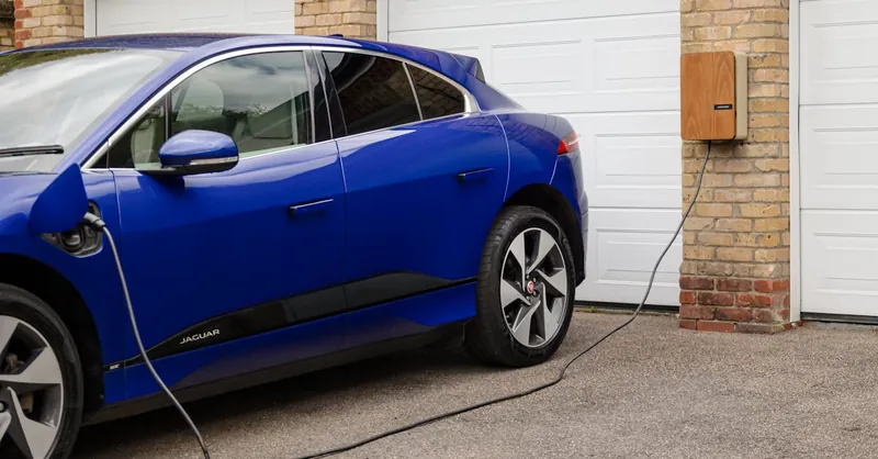 Blue electric vehicle charging at home using wall-mounted unit. Sustainable transportation solution.