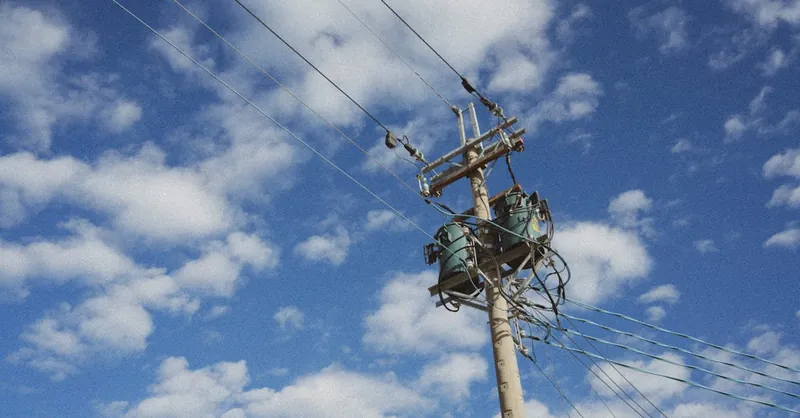 High voltage power lines stretching against a cloud-dappled blue sky, showcasing modern energy infrastructure.