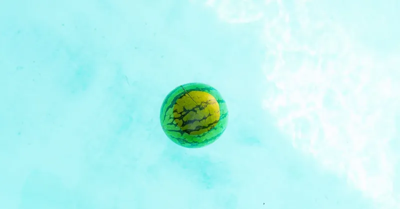 A bright watermelon floats peacefully on a clear blue pool surface.