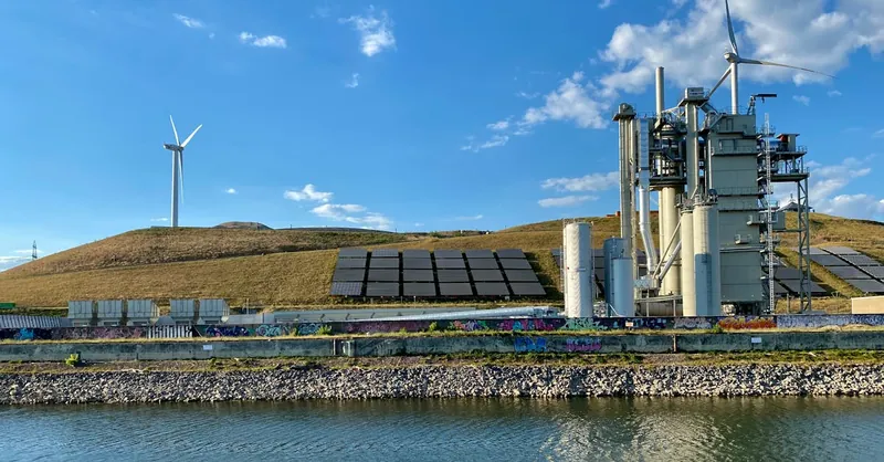 Renewable energy facility in Karlsruhe featuring wind turbines and solar panels beside a river.
