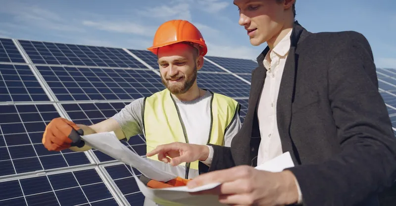 Two engineers reviewing plans for solar panel installation, representing teamwork in renewable energy.