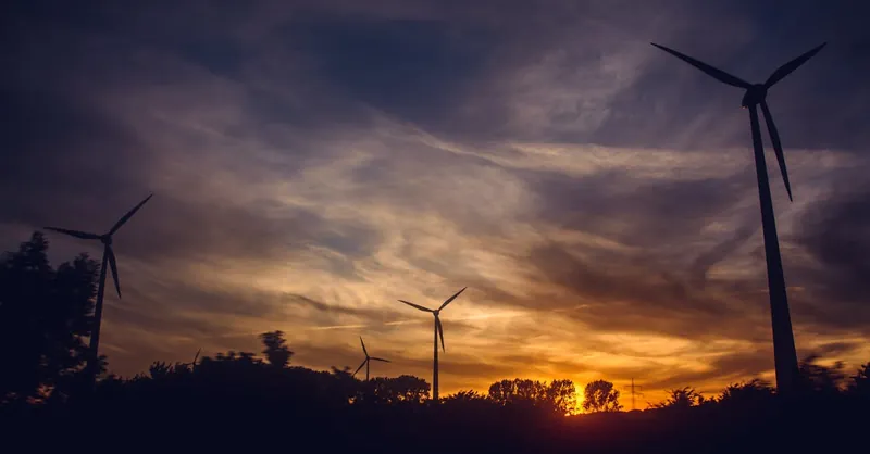 Silhouetted wind turbines at sunset, showcasing renewable energy against a vibrant sky.