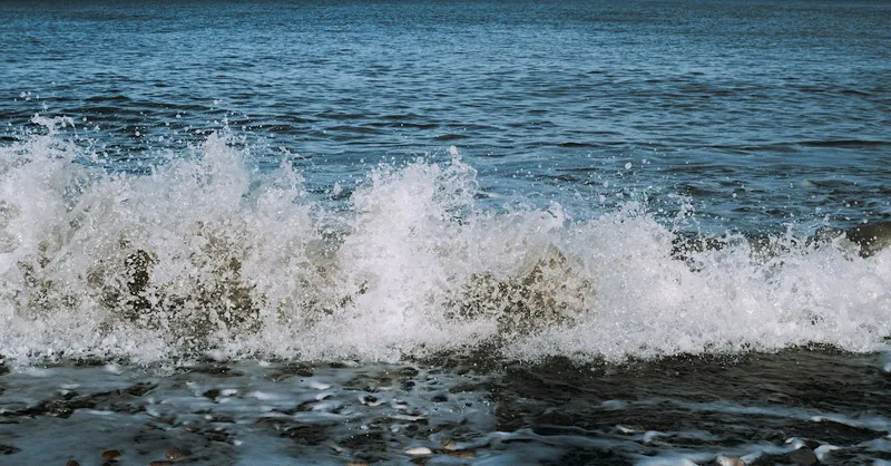Captivating shot of waves crashing with offshore wind turbines on the horizon.