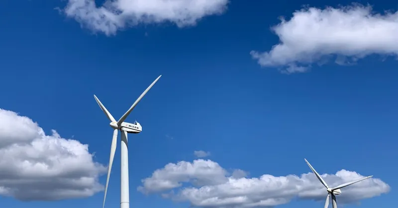 Low angle of white modern windmill turbines generating energy against cloudy blue sky on sunny day