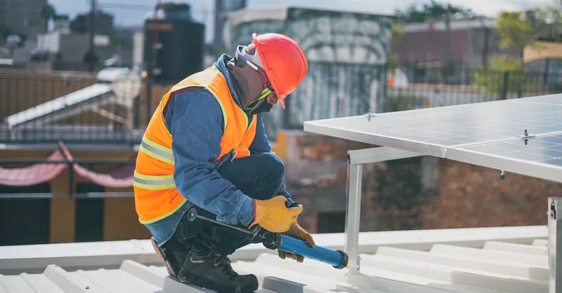 Technician in safety gear installing solar panels on a rooftop, ensuring energy efficiency.