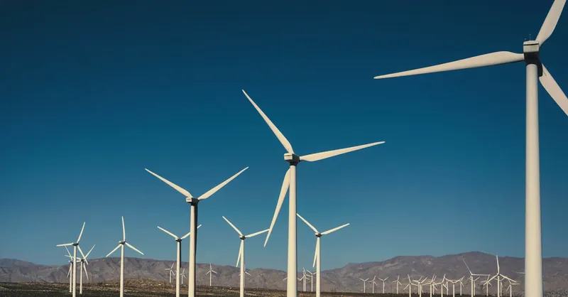 A vast landscape of wind turbines generating clean energy with a backdrop of mountains and a clear blue sky.