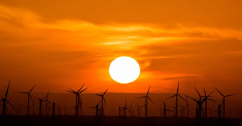 Wind turbines silhouetted against a stunning sunset, showcasing renewable energy in nature.