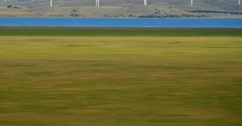 A scenic view of wind turbines near Lake George, Australia, with people walking in the green field.